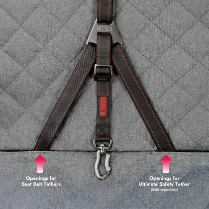 Close-up of a gray quilted pet car seat with black KONG safety harness straps and red stitching, plus overlaid arrows and text indicating seat belt tether openings and separate ultimate safety tether openings.