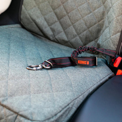 A KONG car seat belt booster and pet leash attachment strap resting on a gray quilted car seat, with a silver metal clasp attached.